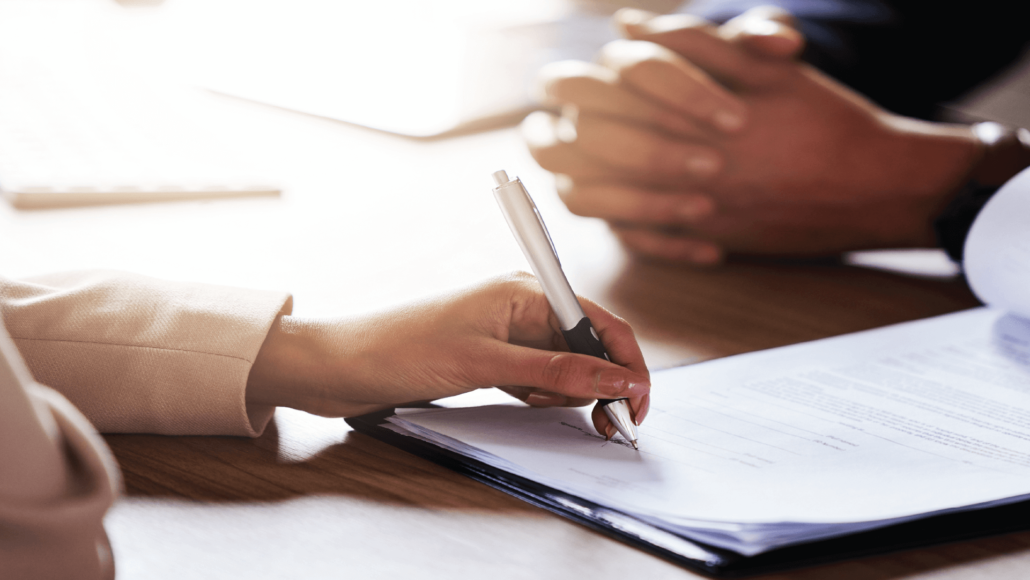 A hand with a pen signing business contracts | IQ Law Group