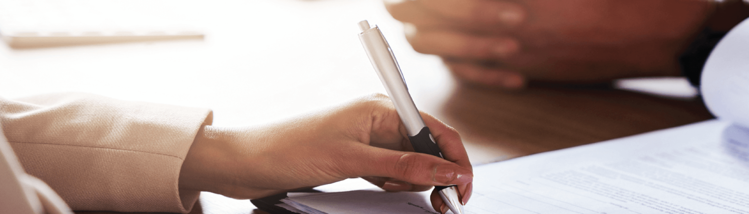 A hand with a pen signing business contracts | IQ Law Group